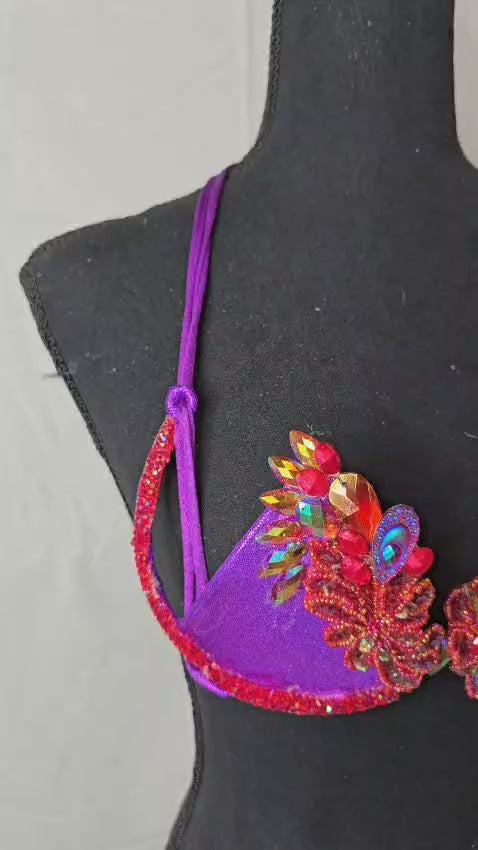 Carnival Orchid Flame Decorated Wire Bra with deep purple fabric, vibrant red and gold floral gem embellishments, and sparkling center crystals, displayed on a black mannequin—perfect for carnival, festivals, and stand-out performances. #CarnivalMW #CarnivalReady #FestivalFashion #WireBra
