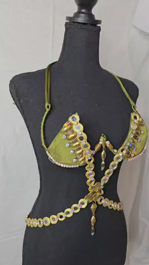 Golden Olive Mirage Decorated Wire Bra featuring olive green cups embellished with gold and iridescent gemstones, a gemstone harness detail, and hanging jewels, displayed on a black mannequin—perfect for festivals, carnivals, and performance wear. #CarnivalMW #FestivalFashion #CarnivalReady #WireBra